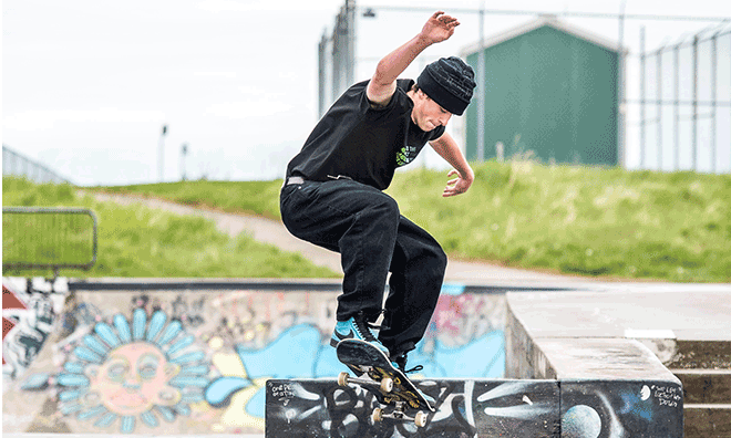 Skateboarder making a maneuver over graffiti art in skate park bowl