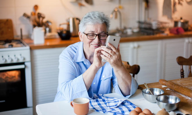 Women sitting in her kitchen using her phone with baking items on the table.
