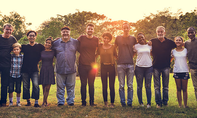 Group of diverse people standing in the park with arms around each others backs.
