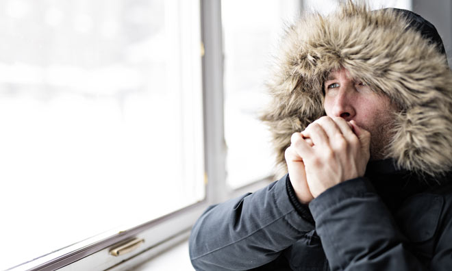 Man in coat blowing on his cold hands
