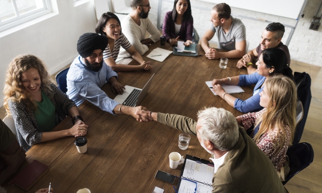 diverse group of people exchange ideas seated around a large boardroom table
