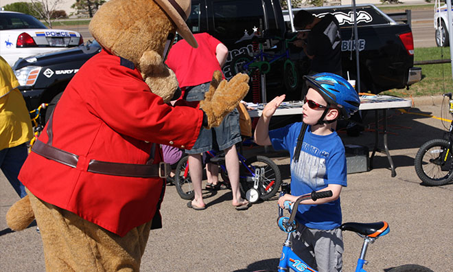 Safety bear giving a high-five to young kid wearing his helmet and holding his bike