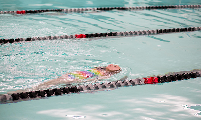 Child in a colourful bathing suit does the backstroke in swimming lanes