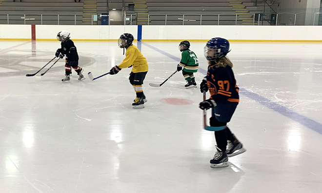 four young children skating in full equipment with various jerseys on