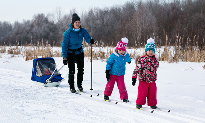 Mother with two daughters cross-country skiing while bundled up in big colourful coats