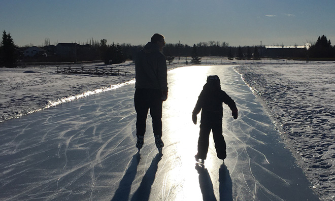 Dad and son skating on a pathway. Vibrant sunlight is shining in front of them which makes them appear as silhouettes
