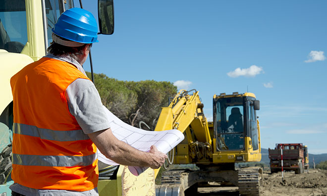 Image of man holding up plans on a construction site