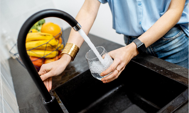 Image of a woman filling a glass of water from the kitchen tap.
